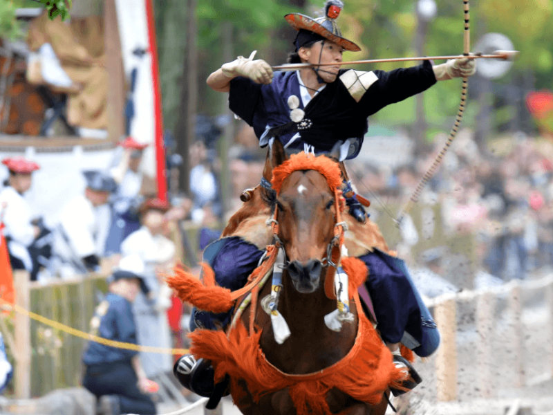 Cavalier en costume traditionnel tirant à l’arc pendant le Yabusame du Reitaisai matsuri — source Japan Travel